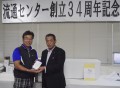 磯哲志さんが優勝（写真左）、新園理事長から賞品を手渡された
