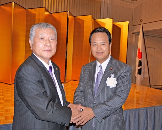甘利明衆議院議員と握手を交わすＪＵＣ喜多俊夫社長（ＪＵ富山理事長）