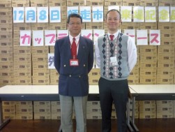 山積みされたカップラーメンの前に立つ大塚会場長