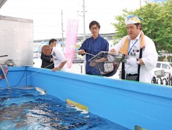 大好評だった『移動釣り堀』　　会員が釣り上げた魚を網ですくい持ち帰りの準備を手伝う営業部の山本真太朗リーダー（写真右）