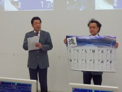 セレモニーでオリジナルカレンダーを紹介するスタッフ（左から秦健二営業室次長と服部祥平主任）
