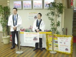 新入社員の２人が１つ１つ会員に来場賞を手渡した