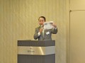 「自動車流通新聞」を手に自己紹介を行う倉元進氏。講演は、総頁３５Ｐのオリジナル資料に基づき行われた